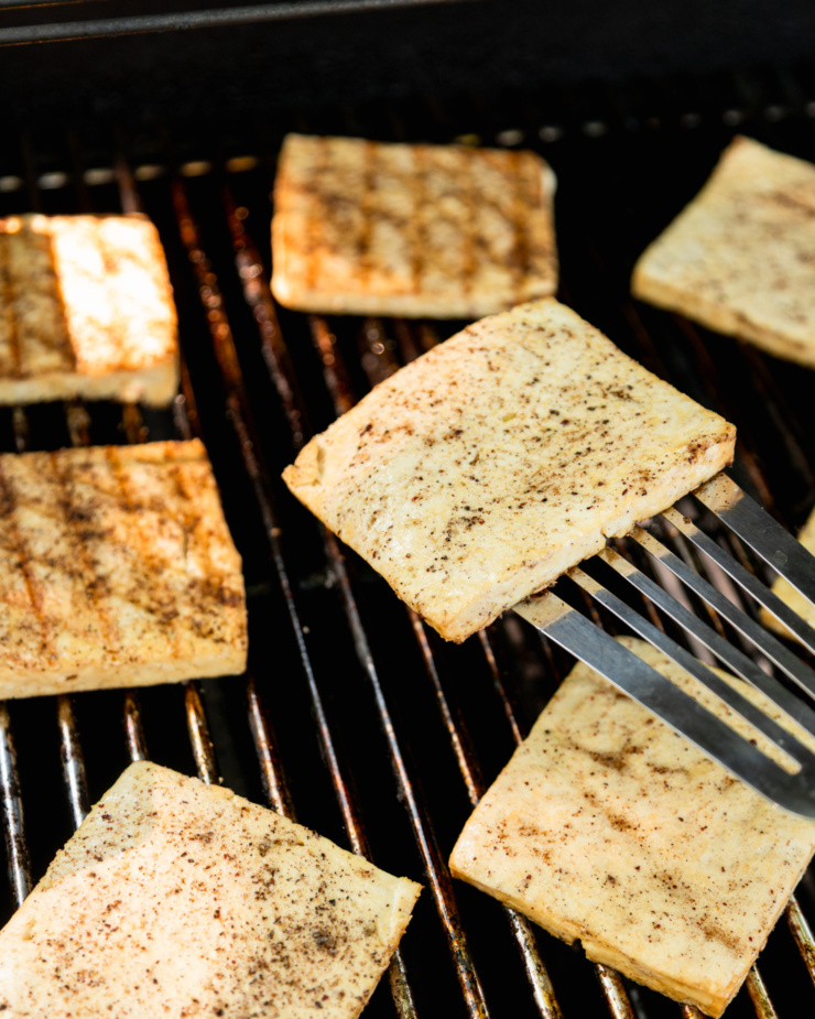 Μια γωνιά 3/4 δείχνει φέτες tofu σε μια υπαίθρια σχάρα.